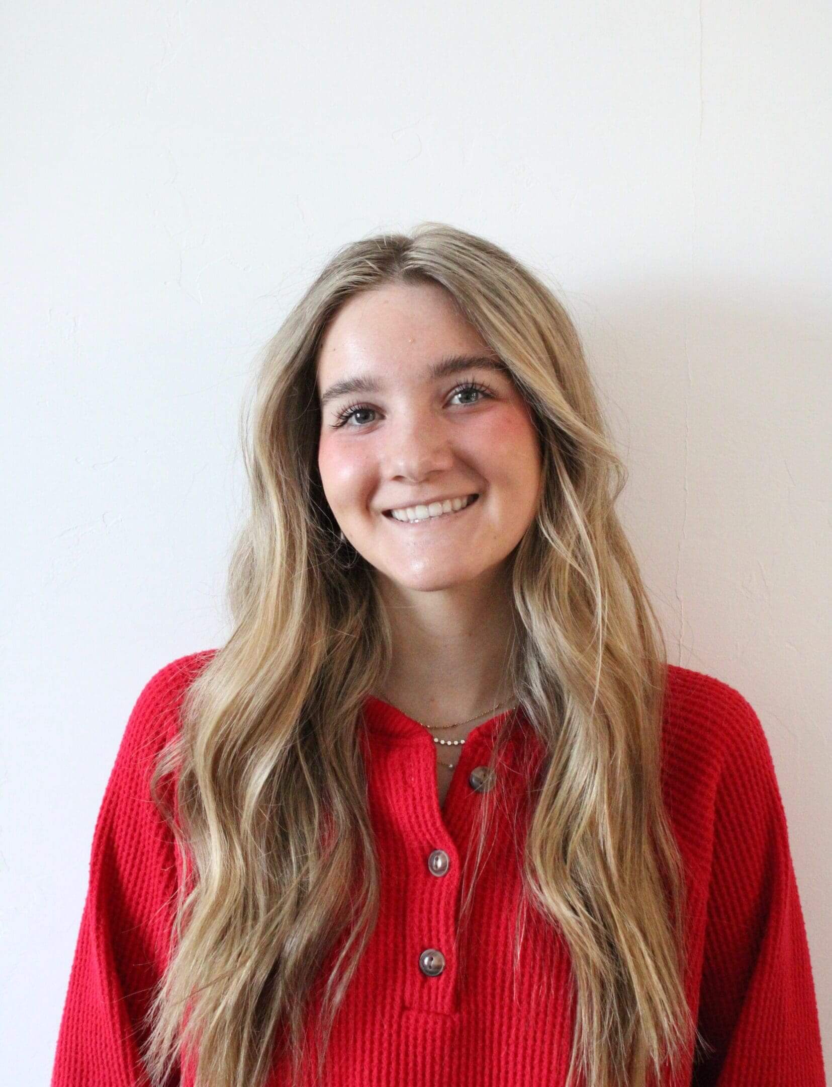 Smiling person with long blonde hair, red sweater